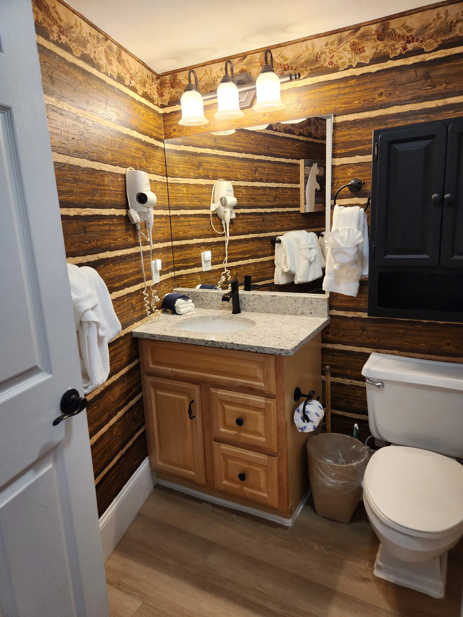 Step into your rustic retreat bathroom with log cabin walls, granite vanity, and plush white robes awaiting your relaxation.