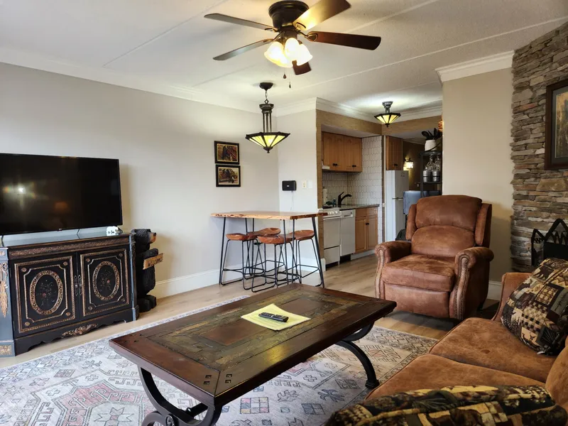 Relax in your cozy living area with rustic leather seating, stone fireplace, and open kitchen—perfect for unwinding after mountain adventures.