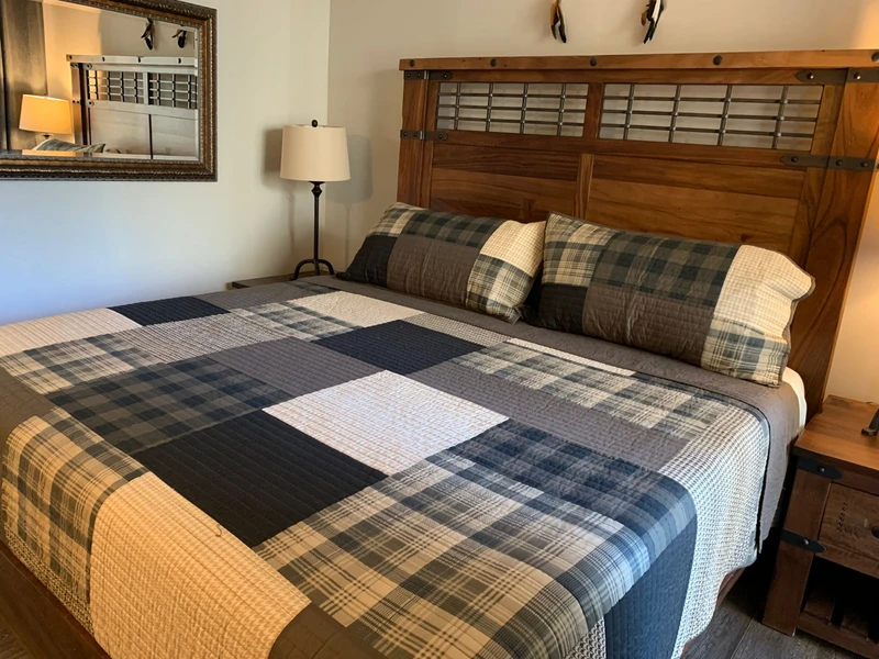 Sink into the rustic king bed with cozy plaid quilting after a day of mountain adventures. The warm wood headboard and soft lighting create the perfect retreat.