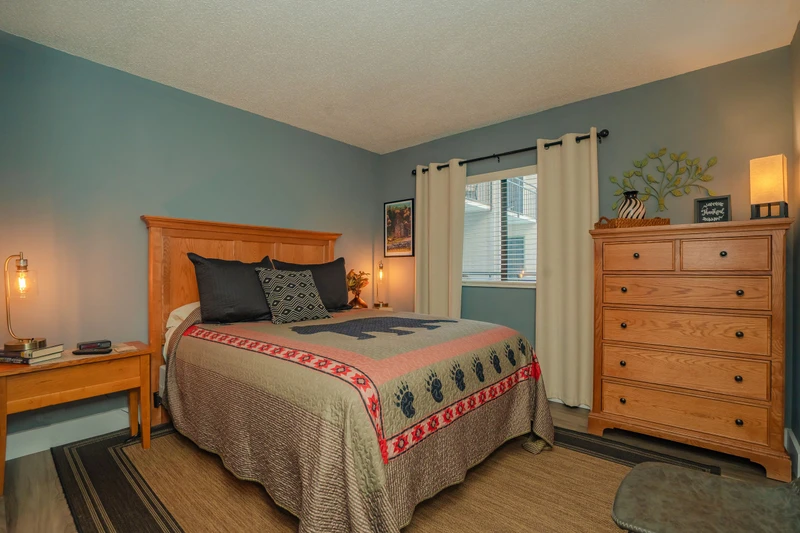 Your serene bedroom retreat features a cozy bed, warm wood furnishings, and calming blue-green walls that invite restful sleep after a day of adventure.