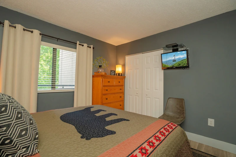 Settle into your cozy bedroom with plush bedding, warm natural light, and scenic mountain views on the wall-mounted TV—your perfect retreat after a day of exploring.