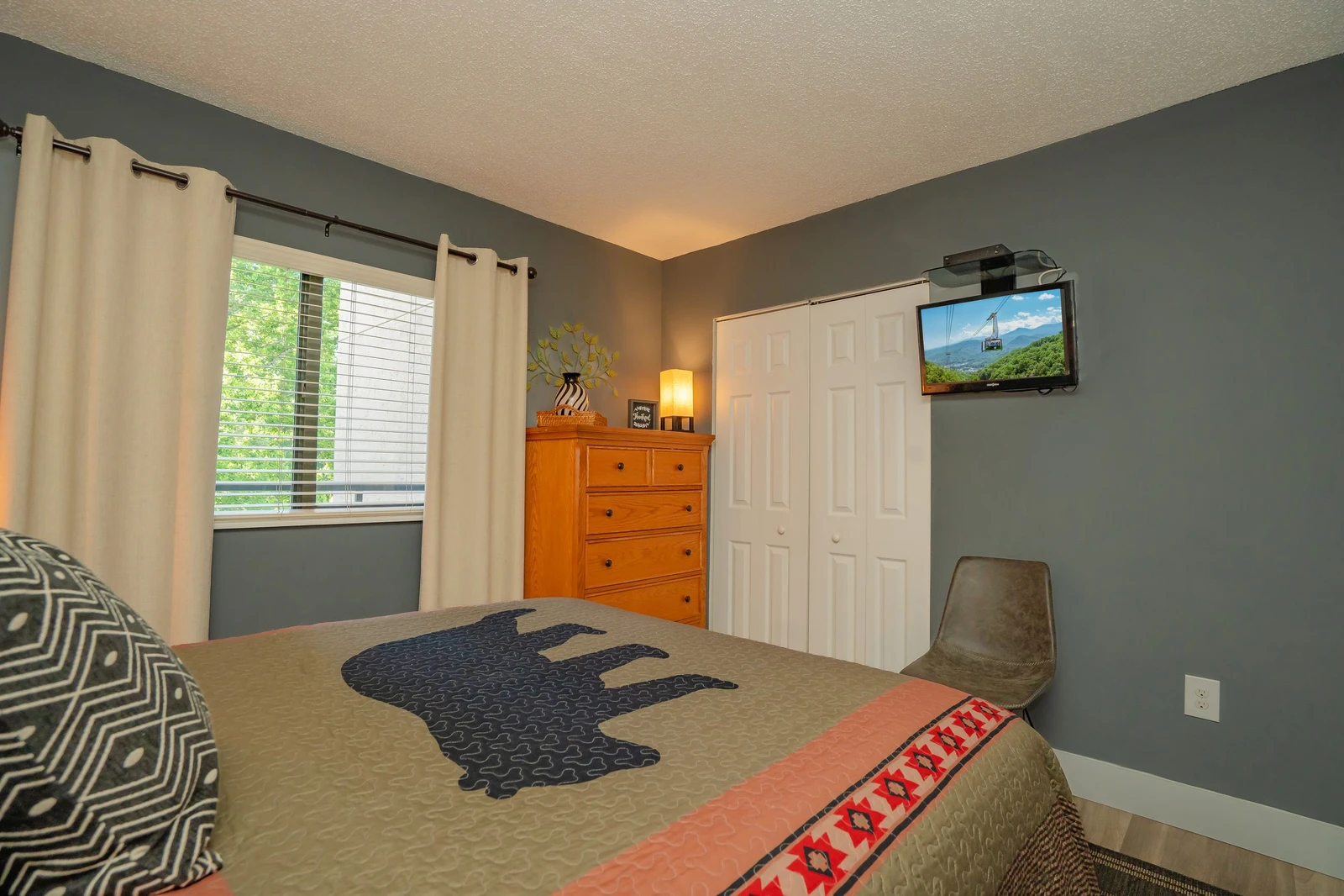Settle into your cozy bedroom with plush bedding, warm natural light, and scenic mountain views on the wall-mounted TV—your perfect retreat after a day of exploring.