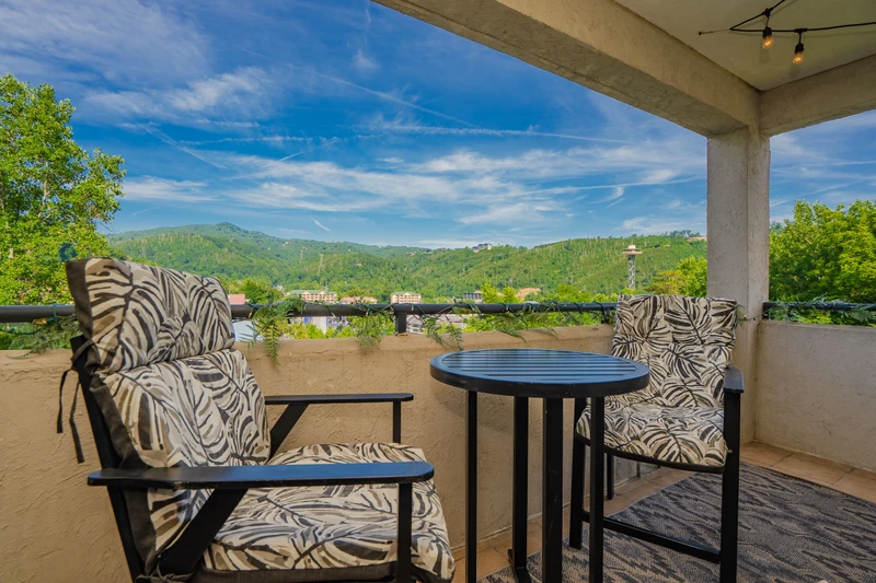 A covered terrace with lush mountain scenery framing the property's location. The outdoor furniture offers seating near town and forested hillsides.