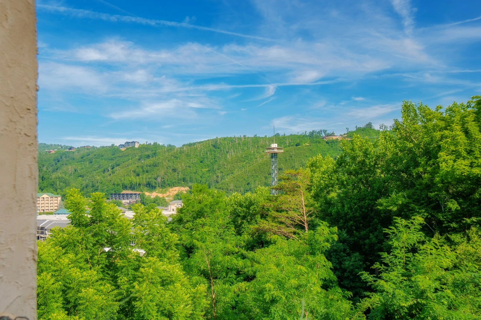 Mountain views framed by lush green forests and a vibrant blue sky, with a distinctive observation tower visible in the valley below, offering a serene natural backdrop.
