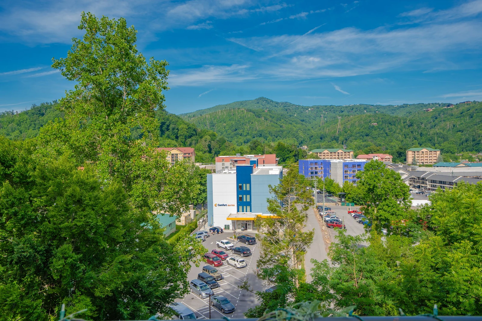 The property sits nestled in a scenic mountain town, with lush green hillsides and neighboring buildings creating a peaceful, vacation-friendly setting.