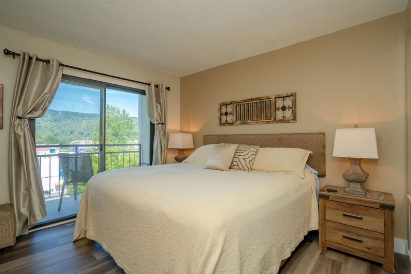 Sink into plush bedding while gazing at stunning mountain views through your private balcony. This serene bedroom blends rustic charm with modern comfort for your perfect escape.