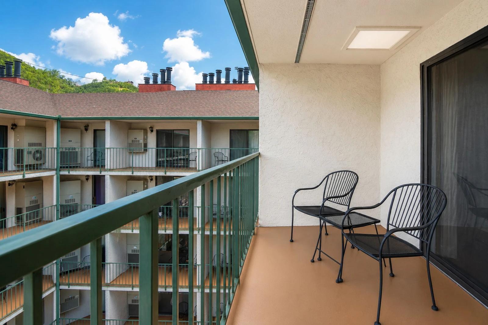The private balcony features two chairs overlooking an interior courtyard, offering a peaceful outdoor spot to relax with morning coffee or evening conversation under open skies.