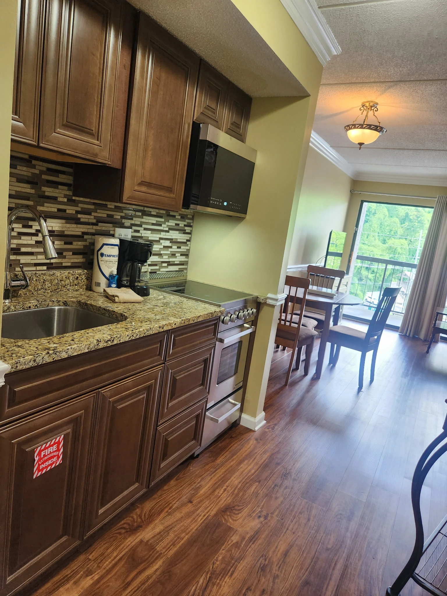 Your fully equipped kitchen flows seamlessly into a bright dining area with balcony access, perfect for preparing meals and enjoying morning coffee with green views.