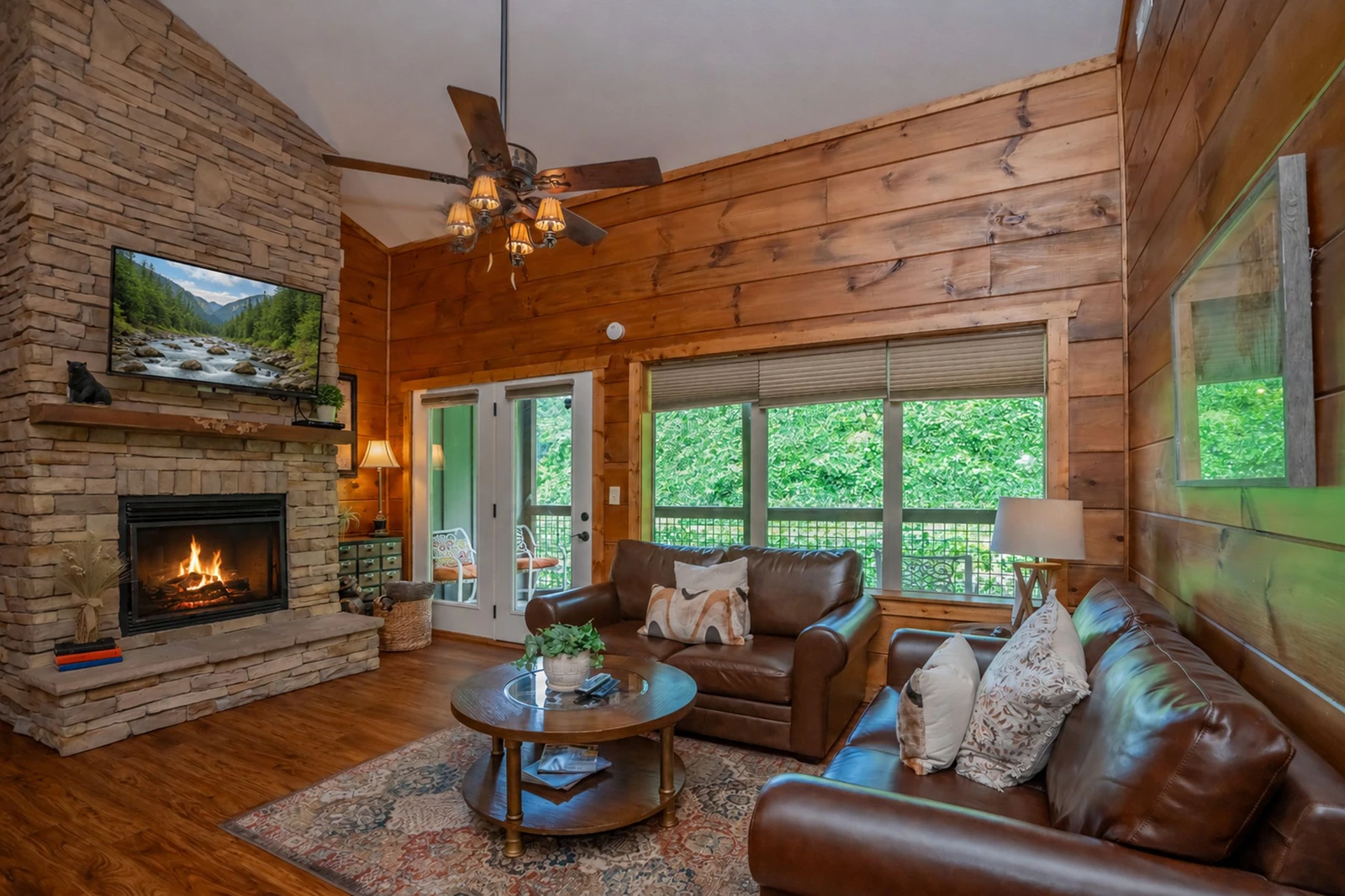 Settle into this warm, inviting living room with rich wood walls, a cozy fireplace, and leather seating perfect for gathering. Large glass doors open to your private deck overlooking lush greenery, creating your peaceful mountain retreat.