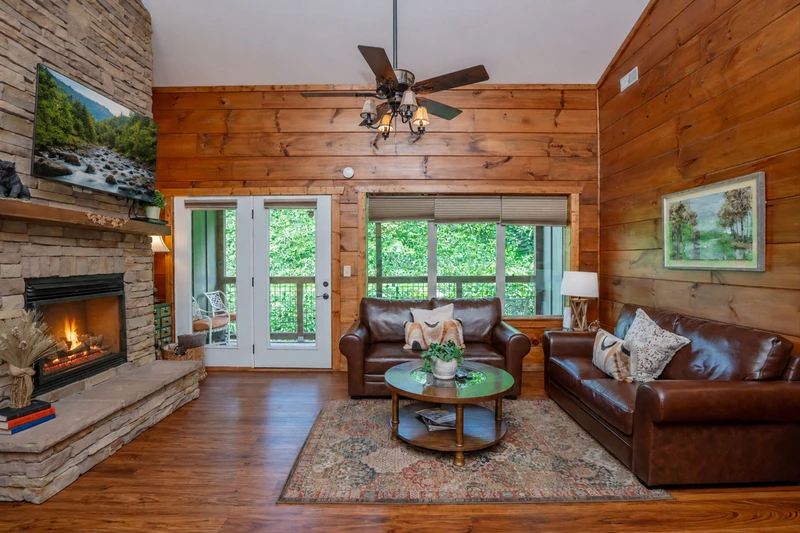 Unwind in your warm cabin living room with rich leather sofas, glowing fireplace, and French doors opening to lush greenery—a perfect retreat after a day of exploring.