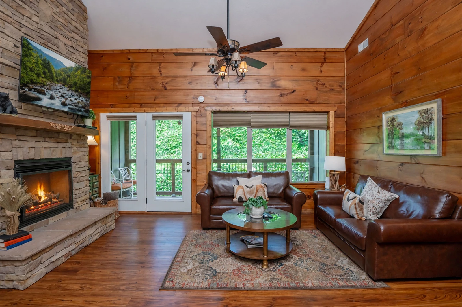 Unwind in your warm cabin living room with rich leather sofas, glowing fireplace, and French doors opening to lush greenery—a perfect retreat after a day of exploring.