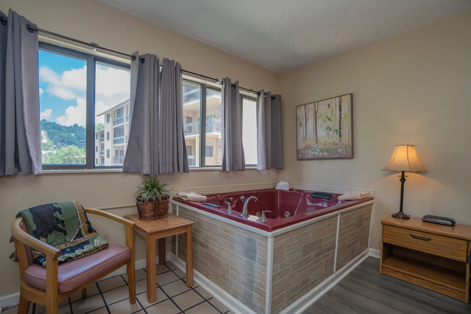 Sink into your private hot tub as sunlight streams through the windows and mountain views frame your retreat. A cozy chair and warm lighting set the scene for ultimate relaxation.