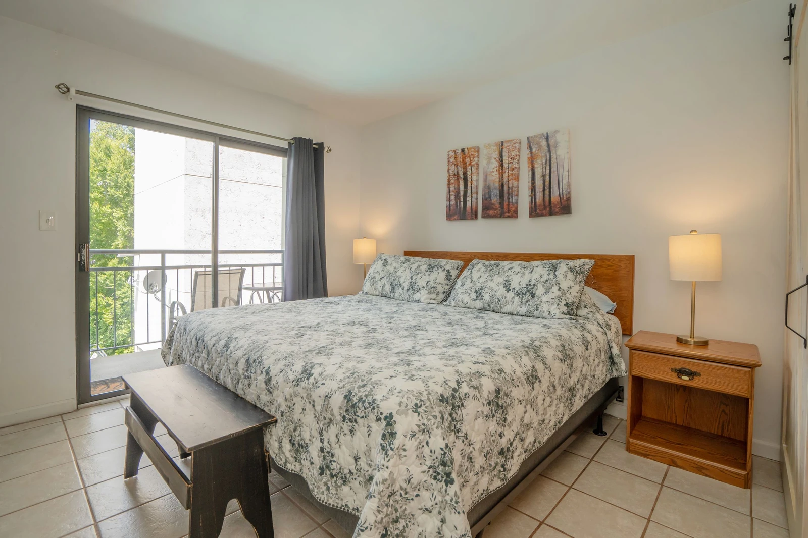 Relax in your cozy bedroom with soft bedding and natural light streaming through the balcony door. Step outside for a breath of fresh air or unwind with the peaceful wooded scene above the bed.
