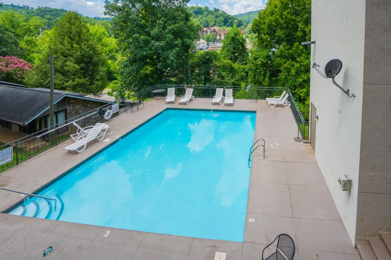 A sparkling pool surrounded by lush trees and mountain views, nestled in a scenic hillside setting. The peaceful surroundings and refreshing water create an ideal retreat.
