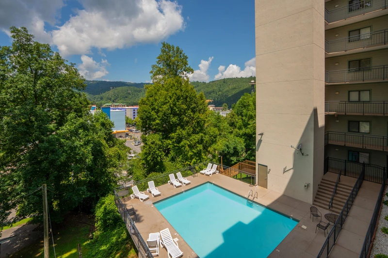 Take in sweeping mountain scenery and the surrounding town from this elevated perspective, with a sparkling outdoor pool and sundeck nestled among towering trees and the multi-story property rising beside it.