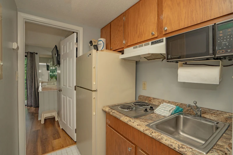 Your compact kitchen has everything you need: a full-size fridge, microwave, electric stove, and stainless sink. Warm wood cabinets and granite-style countertops keep it inviting and practical.
