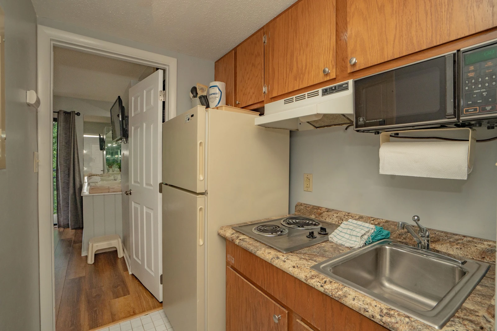 Your compact kitchen has everything you need: a full-size fridge, microwave, electric stove, and stainless sink. Warm wood cabinets and granite-style countertops keep it inviting and practical.