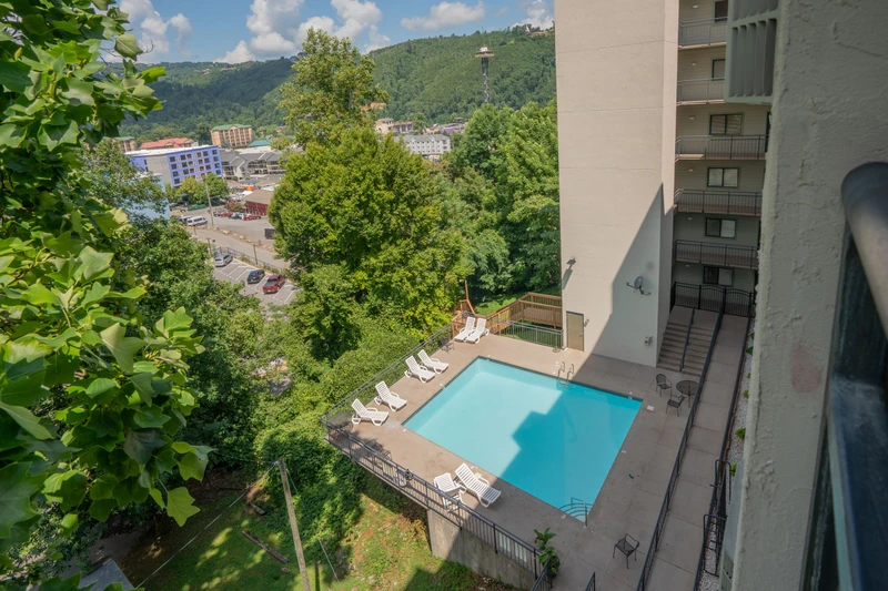 An elevated view showcasing the property's pool area nestled amid lush greenery, with a charming mountain-backed town spread out beyond. The surrounding landscape and nearby buildings frame a peaceful destination for your stay.
