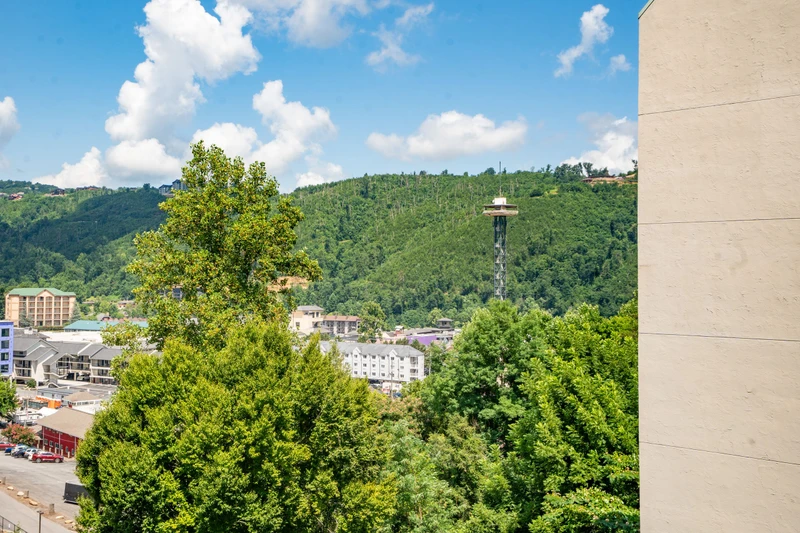 The property sits near downtown Gatlinburg with the iconic Space Needle visible among lush tree-covered hills, offering easy access to local attractions and entertainment.