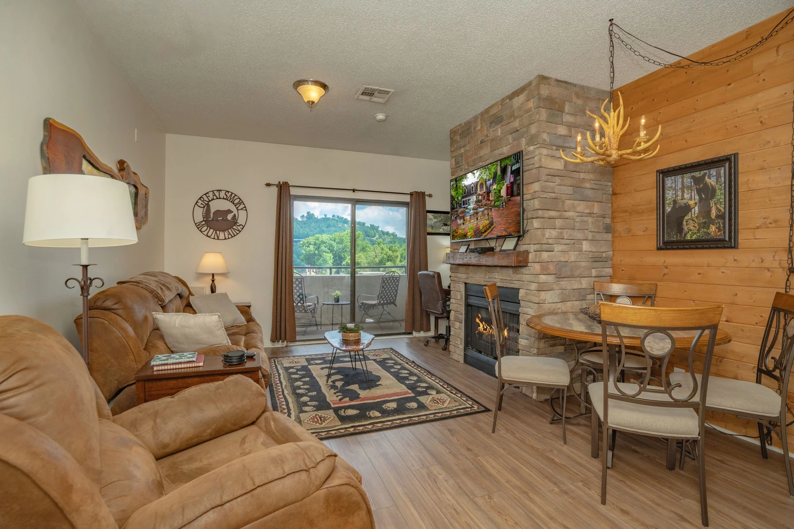 Relax in your cozy living space featuring a stone fireplace, rustic wood accents, and access to your private balcony. The open layout seamlessly connects dining and lounging areas, perfect for unwinding after exploring the mountains.