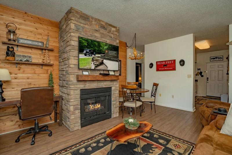 Cozy up by your stone fireplace in this inviting living space, where rustic wood paneling and mountain-themed decor set the perfect tone for your getaway. Relax with your favorite show or share stories around the dining table—your home base awaits.