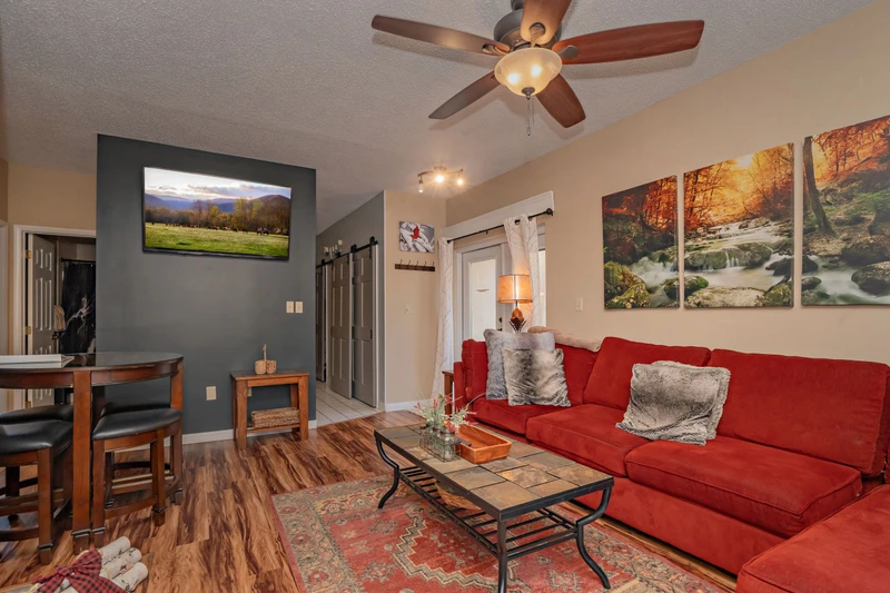 Settle into your cozy living space with a plush red sofa and ceiling fan to keep you comfortable. Natural light and warm tones create an inviting retreat for your stay.