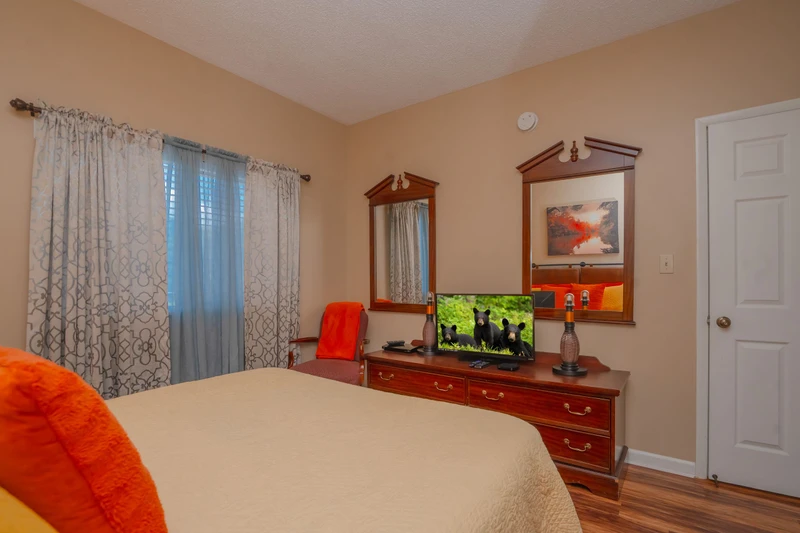Slip into your cozy bedroom with warm wood furnishings, soft bedding, and natural light filtering through patterned curtains. Your private retreat awaits with entertainment and storage for all your vacation essentials.