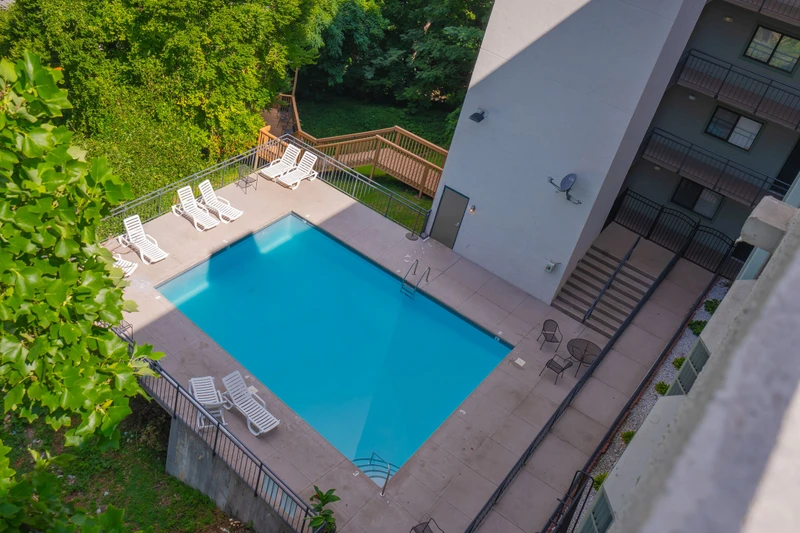 An aerial view of the property showcasing the outdoor swimming pool surrounded by lush greenery and mature trees, with loungers positioned poolside for relaxation.