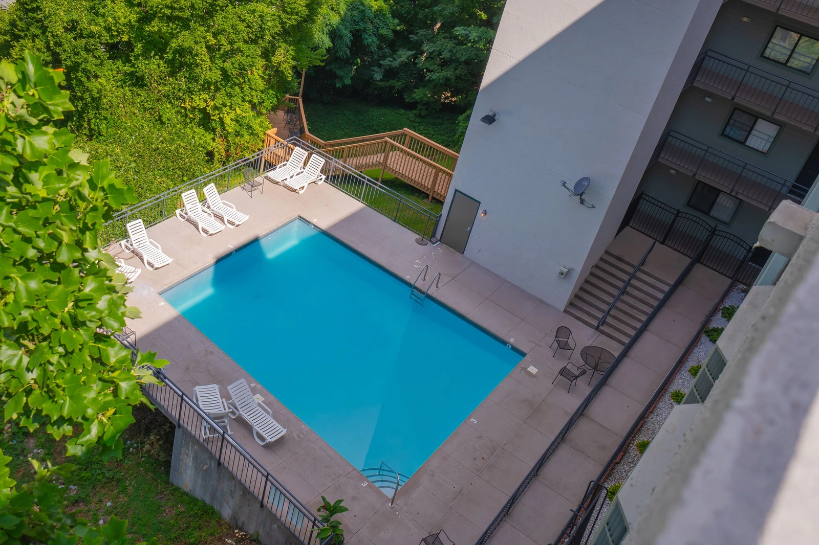 An aerial view of the property showcasing the outdoor swimming pool surrounded by lush greenery and mature trees, with loungers positioned poolside for relaxation.