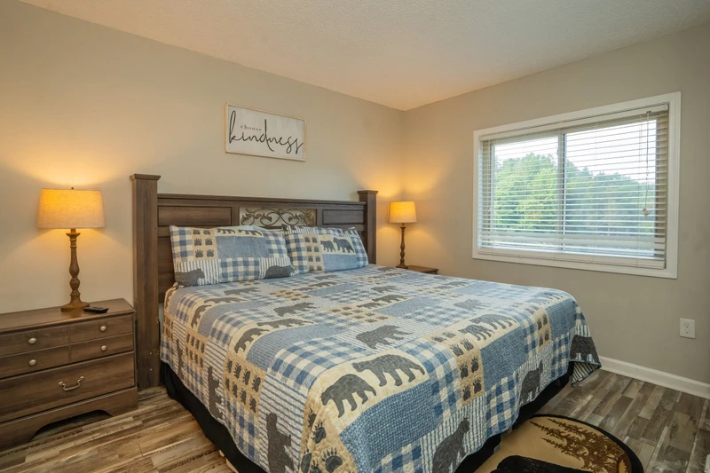 Unwind in this serene bedroom with its plush bedding and warm lighting. Natural light streams through the window, while soft lamps add a gentle glow to help you relax after a day of adventure.