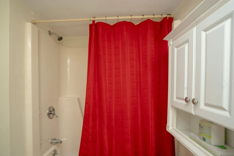 Your private bathroom features a crisp white tub-shower combo with a bold red curtain and thoughtful cabinetry for storing your essentials.