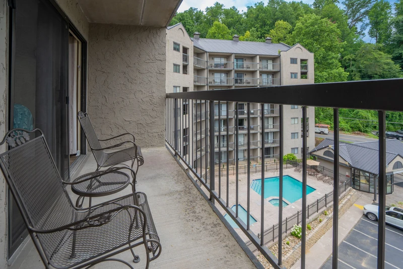 Relax on your private balcony with comfortable seating and enjoy views of the sparkling pool and surrounding trees.
