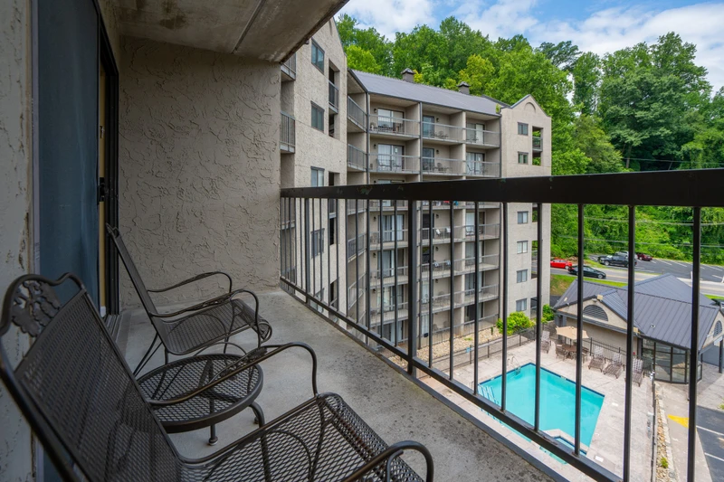Step out onto your private balcony, where two cozy chairs invite you to unwind with views of the sparkling pool below and lush green trees beyond.