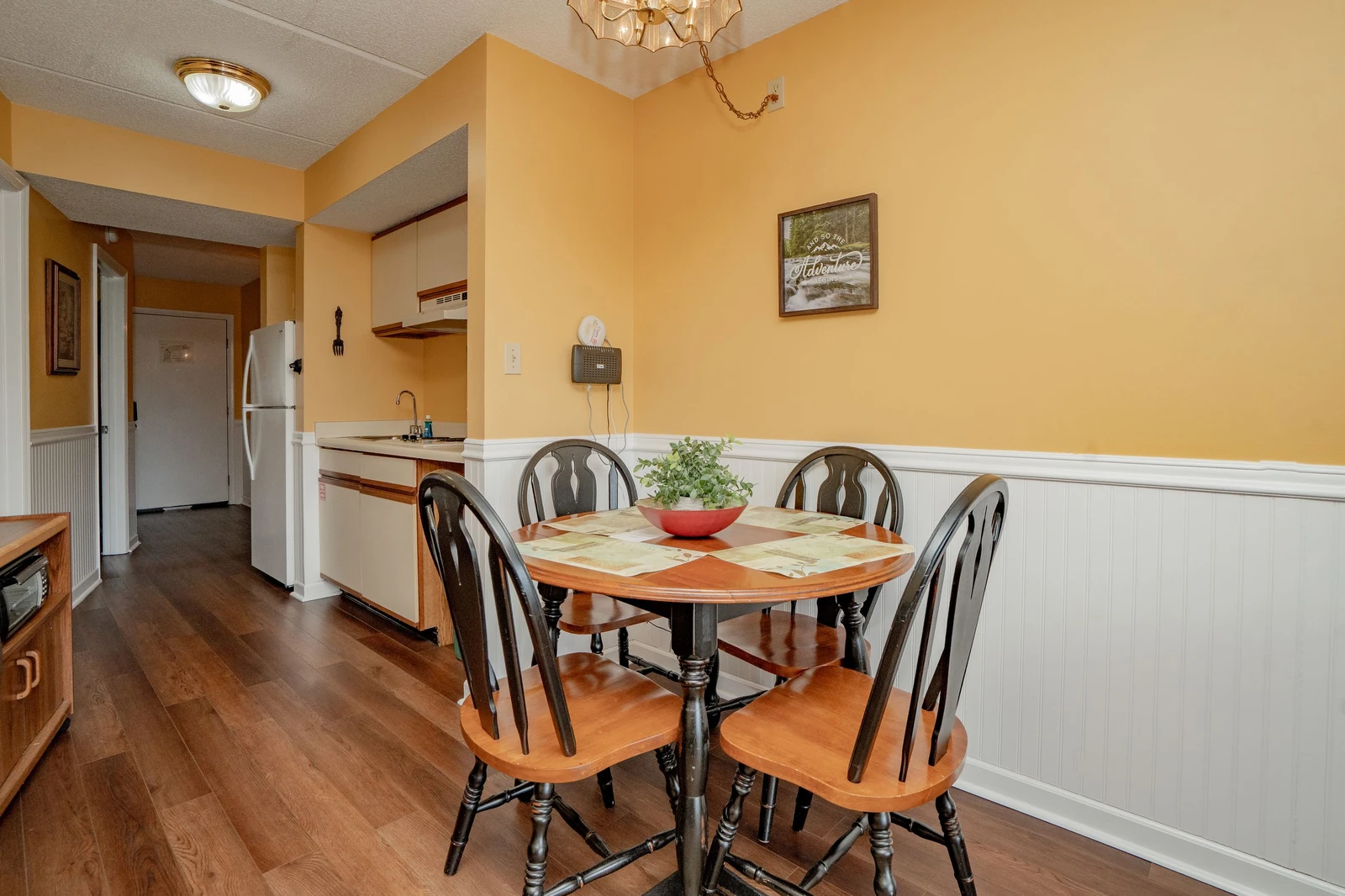 Gather around this welcoming dining table in your cozy kitchen space, warmed by golden walls and natural light—perfect for morning coffee or sharing meals with loved ones.