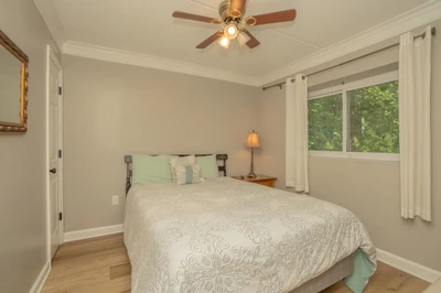 Drift off in your serene bedroom, where natural light filters through windows overlooking lush greenery. The ceiling fan keeps you cool while peaceful treetop views create a calming retreat.