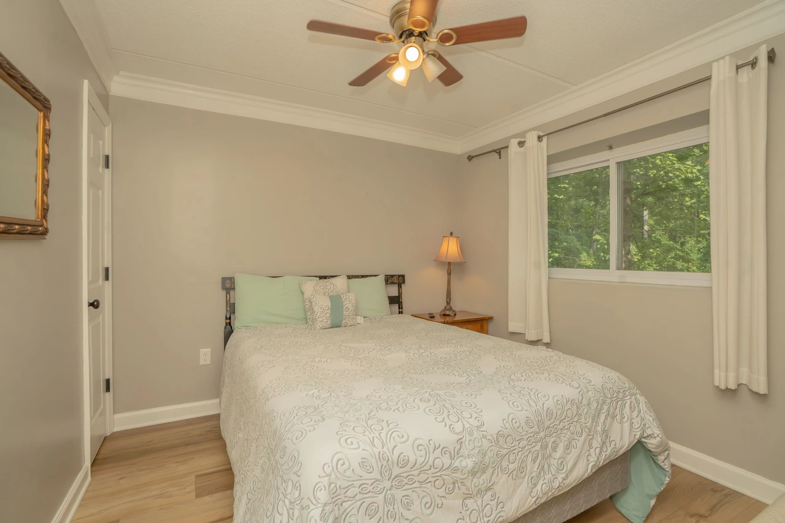 Drift off in your serene bedroom, where natural light filters through windows overlooking lush greenery. The ceiling fan keeps you cool while peaceful treetop views create a calming retreat.