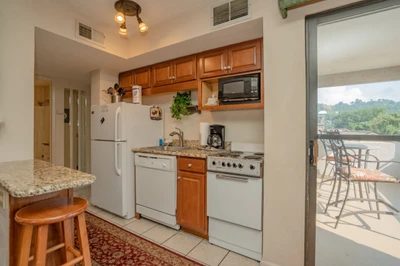 Your fully equipped kitchen has everything you need to prepare meals, with a cozy breakfast bar and doors opening to a private balcony overlooking lush green hills.
