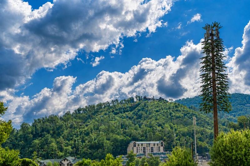 The property sits in the heart of a lush mountain valley, surrounded by rolling forested hills and dramatic cloud-filled skies that define this picturesque area.