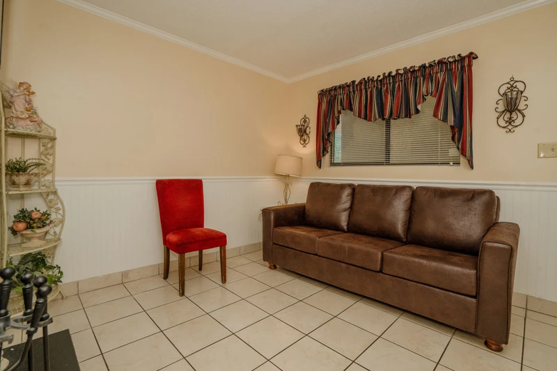 Settle into your cozy living space with a comfortable brown leather sofa and charming red accent chair. The classic tiled flooring and warm tones create a welcoming atmosphere for you to relax after exploring the area.