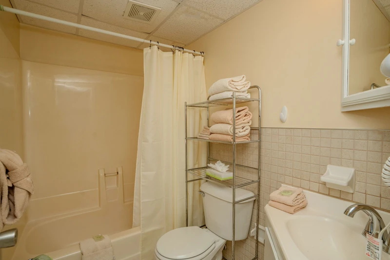Your bathroom awaits with a tub-shower combo, fresh towels neatly arranged on shelving, and all the essentials for a comfortable stay. Simple, clean, and ready for you.