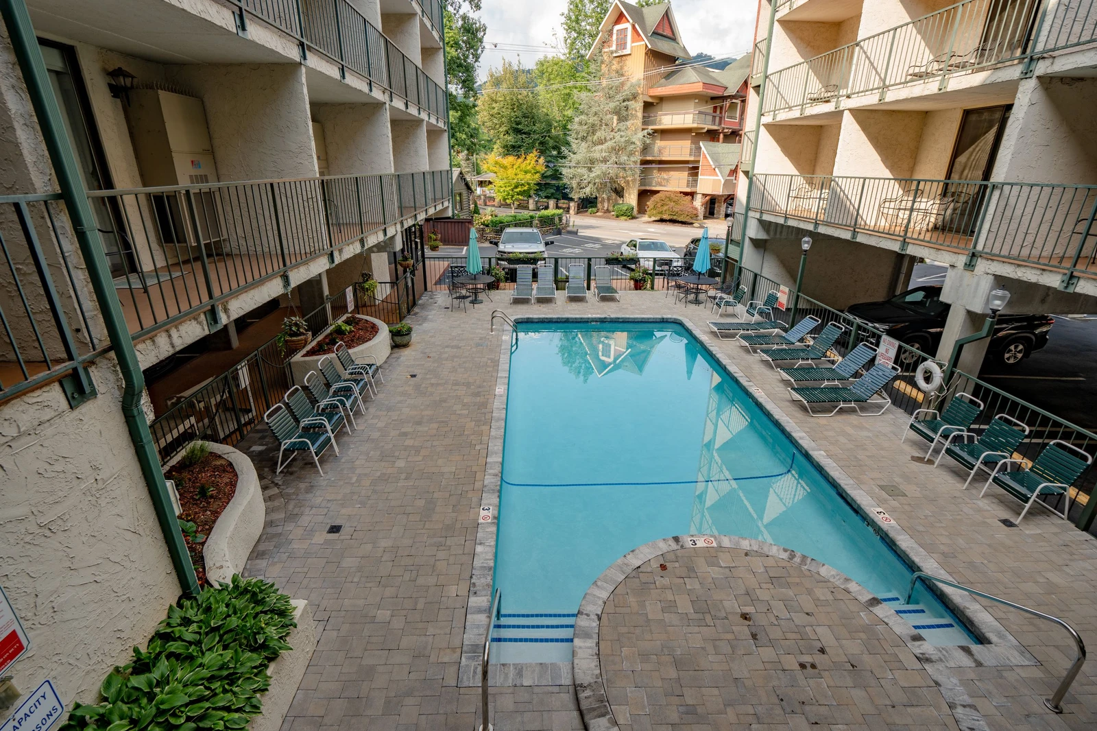 The property features an outdoor swimming pool surrounded by paved courtyard space, lounge seating, and dining areas nestled within the building complex.