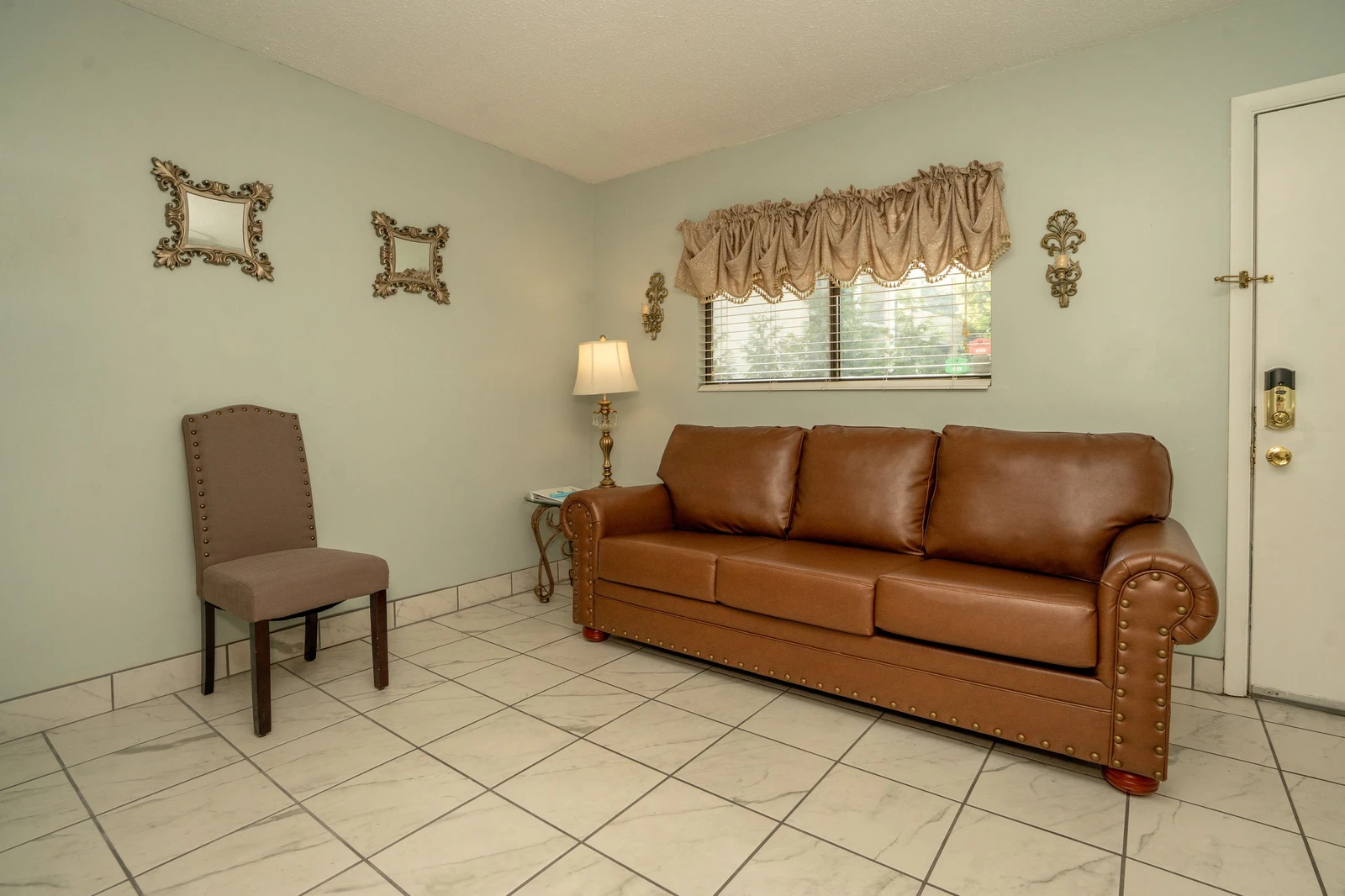 Settle into this inviting living room where a classic leather sofa and cozy chair await your arrival. Natural light filters through the window, creating a welcoming retreat for your stay.