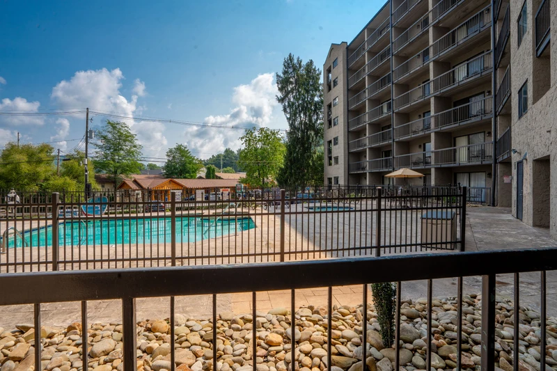 An inviting outdoor pool awaits, featuring a sundeck surrounded by a securely fenced area with lush greenery and blue skies overhead.