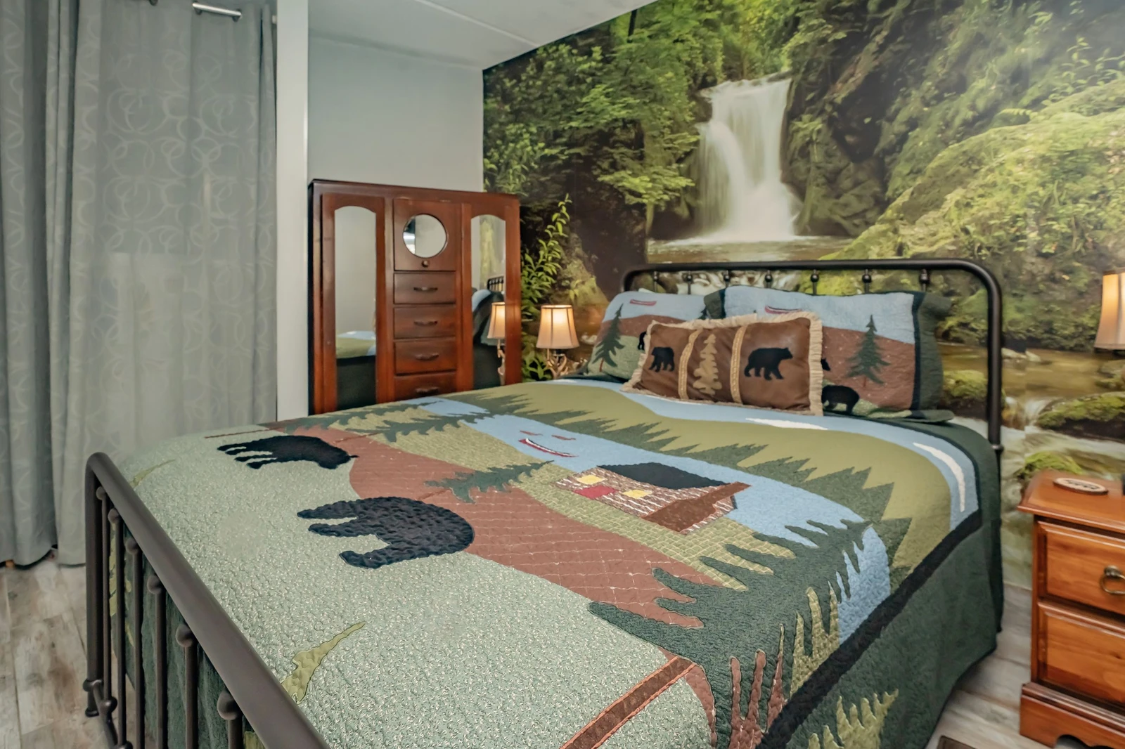 Step into your rustic woodland retreat, where handcrafted quilts and a dramatic forest waterfall mural set the scene for a peaceful mountain escape.