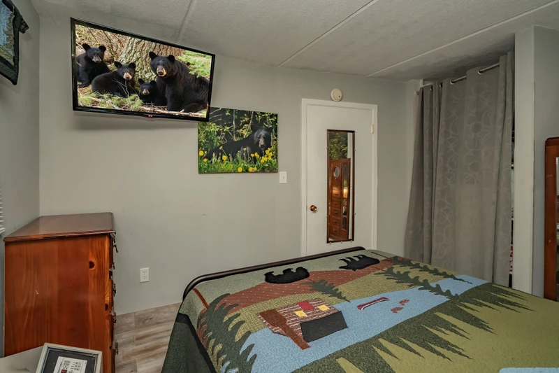 Your cozy bedroom features rustic wood furnishings and a wall-mounted TV for your entertainment. Natural light filters through curtained windows, creating a warm and peaceful retreat after your mountain adventures.