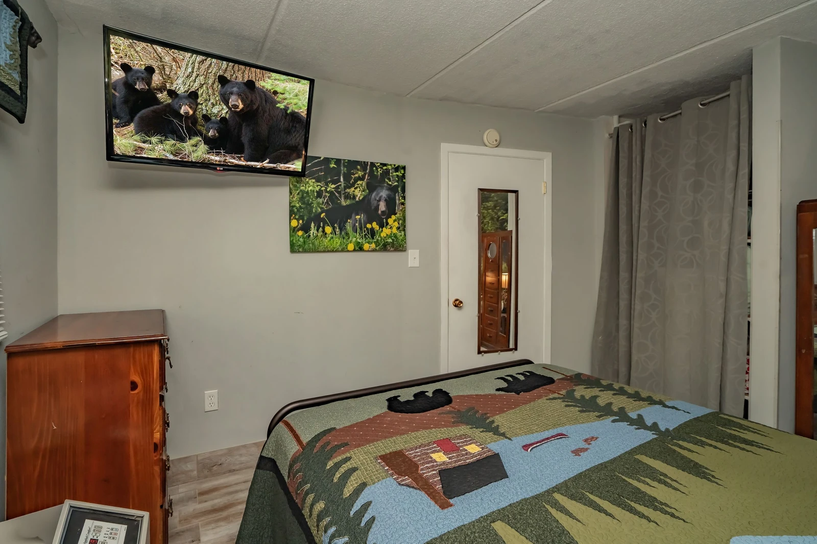 Your cozy bedroom features rustic wood furnishings and a wall-mounted TV for your entertainment. Natural light filters through curtained windows, creating a warm and peaceful retreat after your mountain adventures.