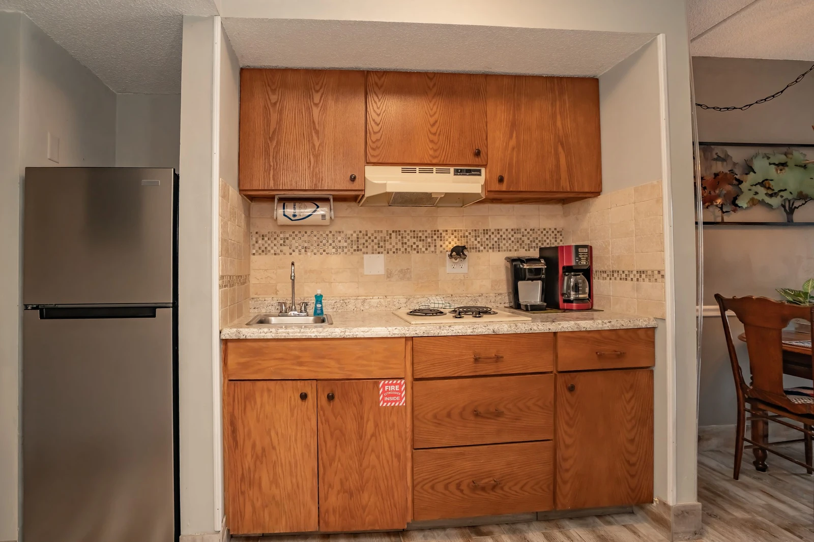 Your compact kitchenette features warm wood cabinetry, a full-size refrigerator, stovetop, sink, and a coffee maker ready for your morning brew—everything you need to feel at home.