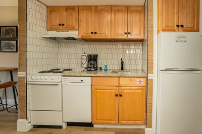 Your kitchenette is equipped with everything you need to prepare meals—a stove, dishwasher, refrigerator, and coffee maker ready for your morning brew. Warm wood cabinetry and charming tile backsplash add a cozy, welcoming touch.