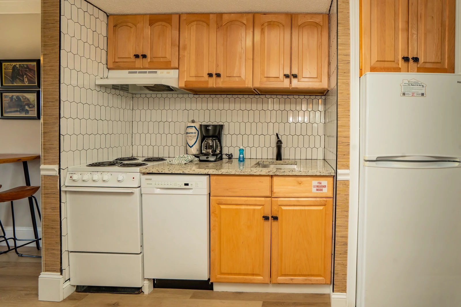 Your kitchenette is equipped with everything you need to prepare meals—a stove, dishwasher, refrigerator, and coffee maker ready for your morning brew. Warm wood cabinetry and charming tile backsplash add a cozy, welcoming touch.