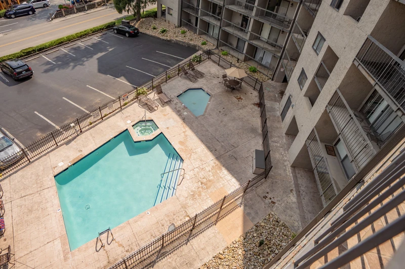 An aerial view of the property's outdoor pool area and parking facilities, surrounded by residential buildings and street access.